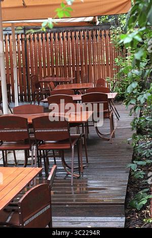 Hölzerne Gartenmöbel im Restaurant und Café - Tische und Stühle auf dem Bürgersteig, umgeben von frischen Pflanzen. Ruhiger Sitzbereich im urbanen Garten, ideal für Stockfoto