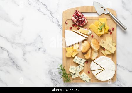 Eine Vielzahl von Käse- und Granatapfelkernen auf einem Holzbrett auf Marmorhintergrund mit Kopierraum. Draufsicht und horizontales Format. Stockfoto