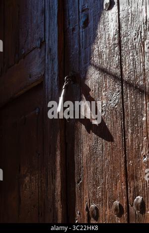 Eine verwitterte Holztür verfügt über einen Vintage-Verschluss, der im warmen Sonnenlicht einen faszinierenden Schatten wirft. Stockfoto