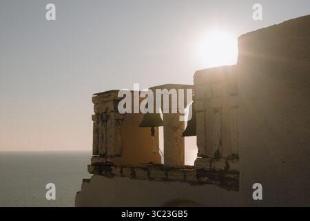Alter Glockenturm mit zwei Bronzeglocken bei Sonnenuntergang, Teil einer traditionellen Kykladen-Kirche mit Blick auf die Ägäis in Santorin, Griechenland. Stockfoto
