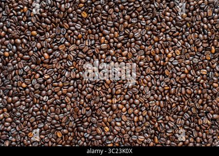 Blick von oben auf frisch geröstete Kaffeebohnen. Großaufnahme von gerösteten Hochglanz-Kaffeebohnen, perfekt für Hintergründe, Café-Branding, Verpackung oder Stockfoto