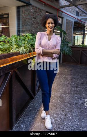 Afroamerikanerin in hellrosa Bluse neben hölzernen Pflanzkästen in der Lobby des Büros Stockfoto