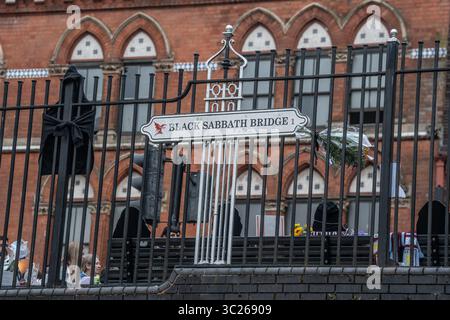 Birmingham, West Midlands, Großbritannien. Juli 2025. Fans versammelten sich im Stadtzentrum von Birmingham an mehreren Orten in der Stadt, um dem Frontmann des Black Sabbath zu Tribut zu zollen, Musik zu spielen, Geschichten auszutauschen oder einfach nur in stiller Betrachtung zu stehen. Im Mittelpunkt stand die Black Sabbath Bridge, wo viele Blumensträuße, Tribut und persönliche Botschaften gelegt wurden. Die Birmingham Central Library wurde als besondere Hommage in lila beleuchtet. Credit Ian Knight/Alamy Live News Stockfoto