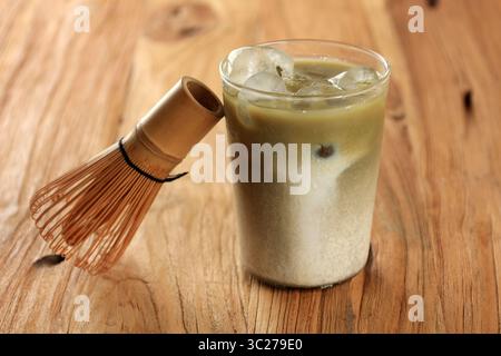 Close Up Grüner Tee Matcha Latte auf klarem Glas über Holztisch mit Chasen Stockfoto