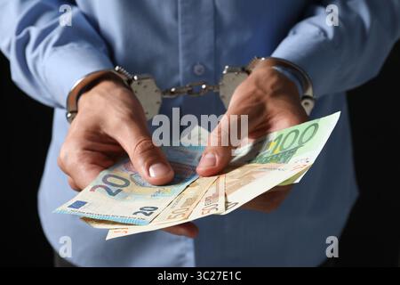 Korruption. Mann in Handschellen, der Euro-Banknoten auf schwarzem Hintergrund hält, Nahaufnahme Stockfoto