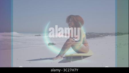 Sitzende Frau in orangefarbenem Bikini, die auf gelbem Surfbrett auf Sand auf das Meer blickt, 0 % digitale Überlagerung Stockfoto