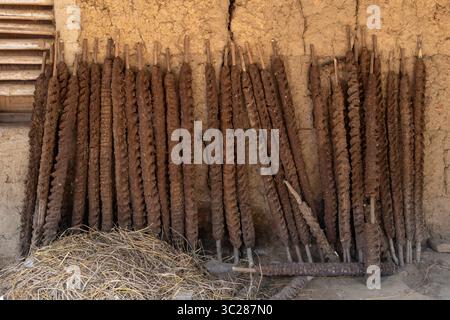 Handgefertigte Kuhmist-Brennstäbe, gemischt mit Stroh und anderen organischen Materialien, werden an einer Schlammwand befestigt, um in einem ländlichen Dorf in Bangladesch zu trocknen. Stockfoto