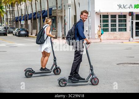 Miami Beach Florida, Washington Avenue, Transport von Elektrorollern, junge Erwachsene, die Roller fahren, Mann Frau Paar auf E-Scootern, Rucksäcke lässig cl Stockfoto