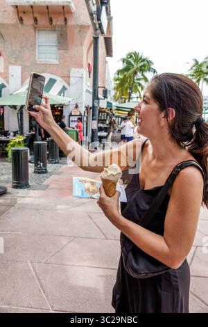 Miami Beach Florida, Espanola Way, hispanische lateinamerikanische Dame, erwachsen lächelnd, fotografierend mit Smartphone Selfie, Eiskegel Dessert Snack, Karte Stockfoto