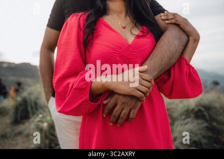 Die intime Umarmung des liebenden Paares. Die Arme des Mannes um die Frau in rotem, sanftem Licht. Ausschreibungsverbindung. Stockfoto