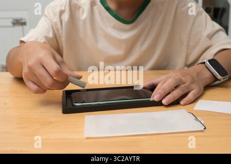 Nahaufnahme einer Person, die mithilfe des Ausrichtungswerkzeugs einen Bildschirmschutz auf dem Smartphone anbringt. Montagevorgang der Schutzfolie auf dem mobilen Gerät für Scratch p Stockfoto