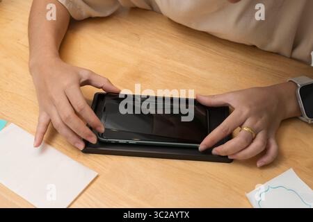 Schließen Sie die Hände, und richten Sie die Schutzfolie aus gehärtetem Glas vorsichtig auf das Smartphone aus. Letzter Schritt der Installation des Bildschirmschutzes. DIY-Prozess zum Keen Stockfoto
