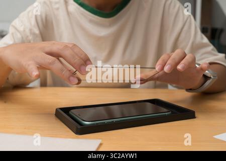 Nahaufnahme einer Person, die den Schutzschirm aus gehärtetem Glas am Smartphone installiert. Letzter Schritt der Anwendung zum Schutz des Geräteschilds vor Kratzern, Staub, Stockfoto