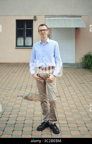 Ein Mann steht selbstbewusst vor einem modernen Gebäude, trägt ein hellblaues Hemd und eine beige Hose. Seine dunklen Schuhe ergänzen das Outfit Stockfoto