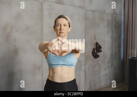 Ein Fitness-Enthusiast macht sich in einem Trainingsraum an Dehnübungen zum Aufwärmen beteiligt. Die Person steht mit nach vorne gestreckten Armen und bereitet sich auf eine vor Stockfoto