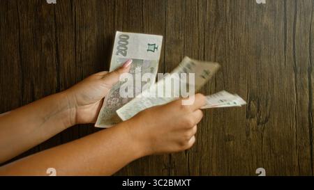 Frau, die tschechische Kronen über einem hölzernen Tischhintergrund zählt und Hände und Finger zeigt, die Geld halten Stockfoto