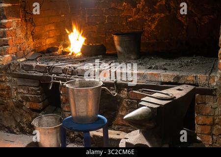 Ein Schmiedemeister in der Arbeit, der Geschichte mit Feuer und Stahl in einer traditionellen Werkstatt schmiedet. Stockfoto