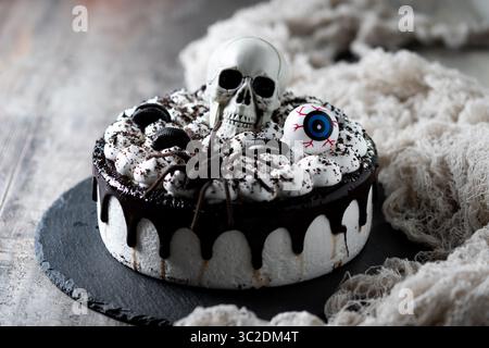 Gruseliger Halloween Schokoladenkuchen mit Totenkopf, Augapfel und Spider Dekoration auf dunklem Hintergrund Stockfoto