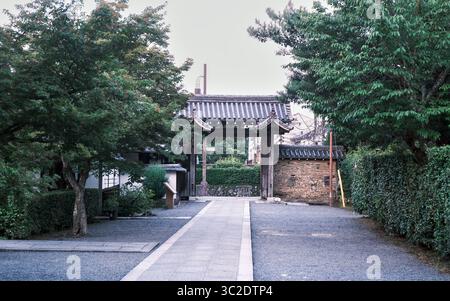 Ein ruhiges, traditionelles Holztor in Kyoto, Japan, umgeben von lebhaften grünen Bäumen und Steinpfaden. Arashiyama, Kyoto, Japan. 07.01.2025. Stockfoto