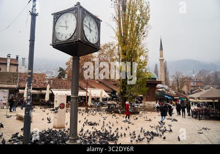 Sarajevo, Bosnien - 2. Dezember 2022: Bezaubernde Uhr auf einem wunderschönen und pulsierenden Stadtplatz voller Tauben und Menschen Stockfoto