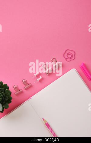 Blick von oben auf den Schreibtisch mit rosafarbenem Schreibpapier und offenem Notizblock. Platz für Ihren Text. Stockfoto