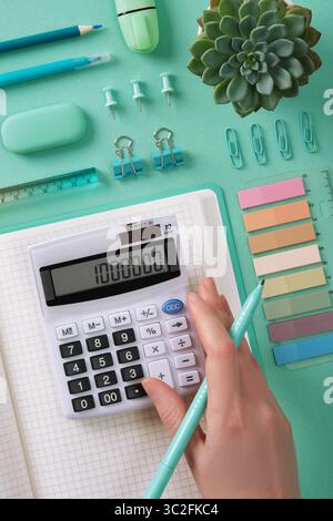 Organisierter Arbeitsplatz mit Bürobedarf im mintgrünen Design. Die Hand einer Frau drückt Knöpfe am Rechner. Stockfoto