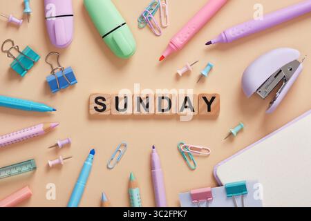 Word Sunday aus Holzblöcken mit bunten Pastell-Schreibwaren auf beigem Hintergrund Stockfoto
