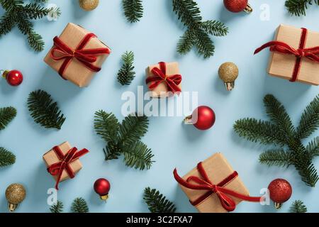 Festlicher Hintergrund mit kleinen Geschenkboxen, die in Kraftpapier gewickelt sind, mit Schleifen aus rotem Samtband, hellgrünen Kiefernzweigen und roten und goldenen Weihnachten o Stockfoto