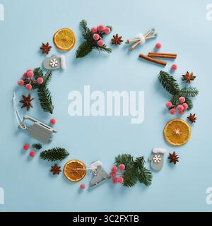 Runder Rahmen aus Tannenzweigen, getrockneten Orangen, Anissternen und Weihnachtsspielzeug auf hellblauem Hintergrund. Platz für Ihren Text. Stockfoto