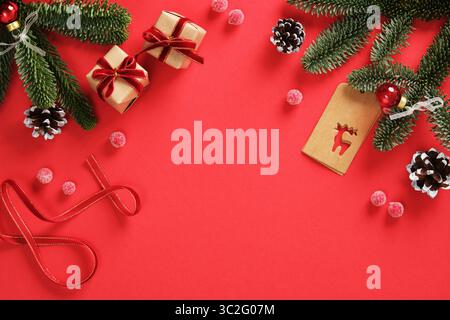 Weihnachtshintergrund mit kleinen Geschenken, Zweigen von immergrüner Tanne, Kegel, Band und Tags auf rotem Hintergrund. Platz für Ihren Text. Stockfoto
