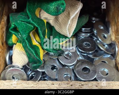 Eine Holzkiste mit glänzenden Metallscheiben sitzt neben einem Paar grüne und gelbe Handschuhe. Die Einstellung zeigt einen gut genutzten Arbeitsbereich, was darauf hindeutet Stockfoto