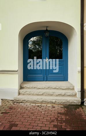 Blaue Tür mit einem weißen Torbogen. Die Tür ist aus Holz und hat ein Glasfenster. Der Bogengang ist aus Stein und hat eine Leuchte. Die Tür ist die Stockfoto