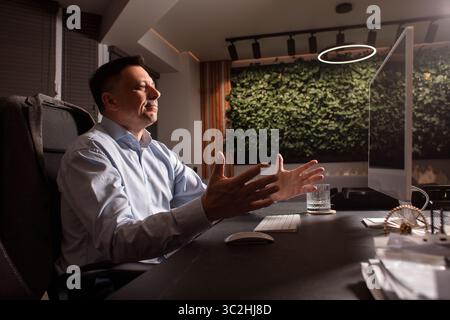Ein verärgerter Geschäftsmann hebt frustriert die Hände, während er an einem überdachten Schreibtisch arbeitet. Symbol für Burnout, Arbeitsstress oder Kündigung. Am Arbeitsplatz. Stockfoto