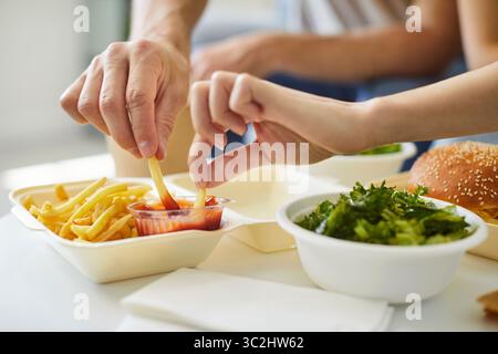 Nahaufnahme von zwei Händen, die Pommes frites in einen Behälter mit Ketchup tauchten Stockfoto