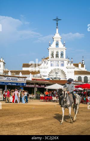 Reiter reiten in einer Straße mit Ermita de la Virgen del Rocio im Hintergrund, El Rocio, Huelva, Andalusien, Spanien Stockfoto