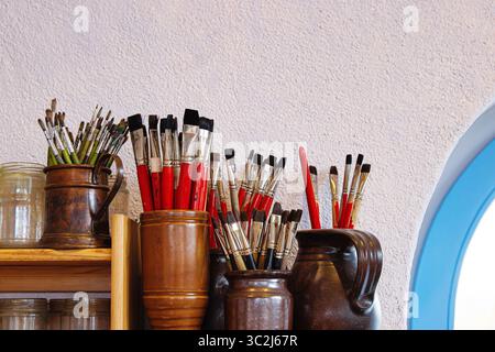 Ein Holzregal im rustikalen Künstlerstudio oder in einer Kreativwerkstatt mit Glasgläsern und Tonkannen, die mit Pinseln gefüllt sind Stockfoto