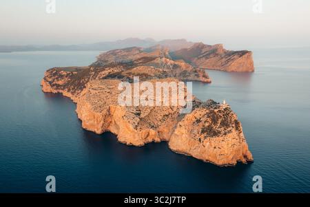 Aus der Vogelperspektive auf die zerklüftete Halbinsel Cap de Formentor, die sich dramatisch in das tiefblaue Meer erstreckt, mit einem kleinen Leuchtturm an der Spitze, Formentor, Balearen, Spanien. Stockfoto
