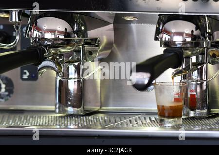 Cremona, Italien - 21. Juli 2025 Nahaufnahme einer professionellen Espressomaschine, die reichhaltigen dunklen Kaffee in zwei kleinen Glasbechern auf einer Edelstahlkarosserie zubereitet Stockfoto