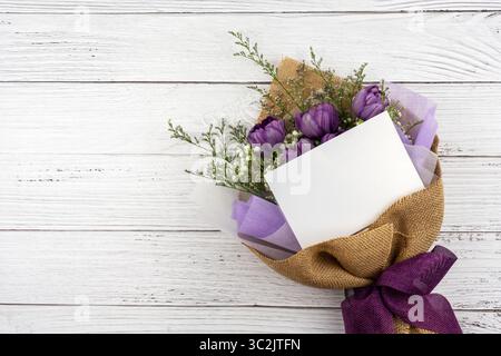 Lila Blumenstrauß mit leerer Grußkarte auf hölzernem Hintergrund Stockfoto