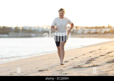 Frau, die barfuß am Strand bei Sonnenuntergang läuft: Gesundheit und Wellness durch Bewegung fördern Stockfoto