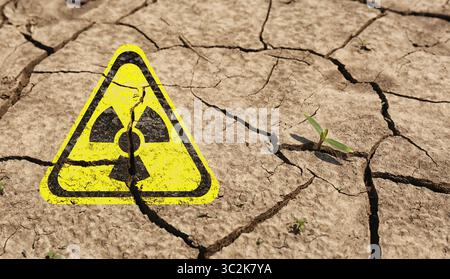 Gelbes radioaktives Zeichen auf gerissener trockener Erde, Nahaufnahme. Radiologische Verschmutzung Stockfoto