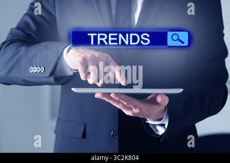 Geschäftsmann mit Tablet-Computer, um heiße Tendenzen, neue Ideen, beliebte Wegbeschreibungen und Nahaufnahmen zu finden. Suchleiste mit dem Wort Trends Stockfoto