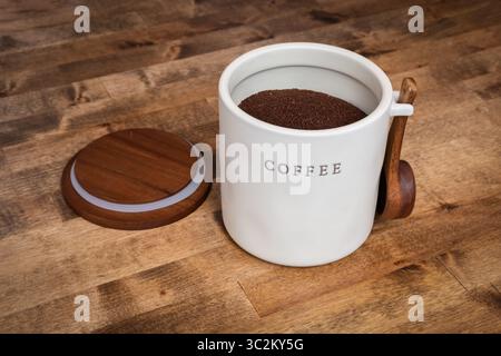 Eine warme, einladende Küchenszene mit einem Keramikkanister mit der Kennzeichnung KAFFEE gefüllt mit gemahlenem Kaffee. Der Behälter befindet sich auf einer rustikalen Holzoberfläche Stockfoto