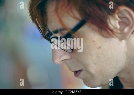 Cremona, Italien - 21. Juli 2025 Nahaufnahme Porträt eines Künstlers mit rot gefärbtem Haar und Brille, der sich intensiv auf ihre Arbeit konzentriert Stockfoto
