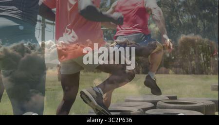 Vier Athleten mit Traktorreifen bei der Reifenbeweglichkeitsübung auf dem grasbewachsenen Parkfeld. Fitness, Training, Teamwork, Outdoor, energiegeladen, motiva Stockfoto