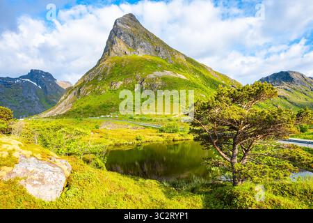 Blick auf den Volandstinden Berg und den kleinen See in grüner Sommerlandschaft in der Nähe des Dorfes Ramberg, Lofoten Inseln, Norwegen Stockfoto