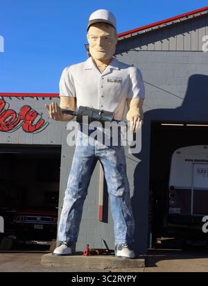 Ein klassischer Schalldämpfer hält einen echten Schalldämpfer in Cookeville, Tennessee, und steht hoch wie eine Straßenfigur mit praxisnahem Reparaturansatz. Stockfoto