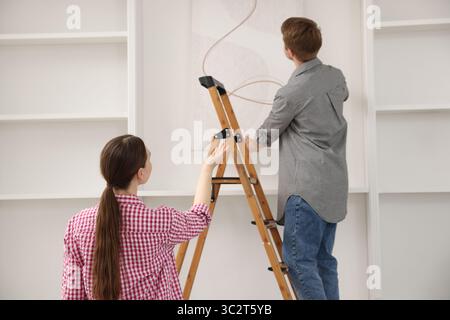 Paare, die zu Hause mit einer Leiter Malerei an die Wand legen Stockfoto