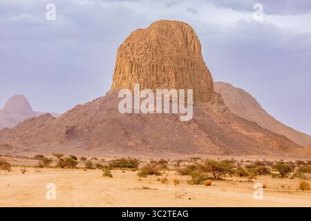 Ein atemberaubender Blick auf den Mount Ilamane, eine massive vulkanische Felsformation, die aus dem goldenen Sand der algerischen Sahara ragt. Die Pastelltöne des d Stockfoto