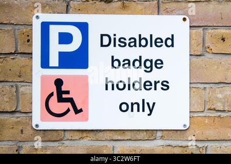 Nur für Behindertenausweishalter ist ein an einer Ziegelwand angebrachtes Parkschild mit Hinweis auf eingeschränkte Parkmöglichkeiten für Inhaber blauer Ausweisschilder in einem ausgewiesenen Bereich. Stockfoto